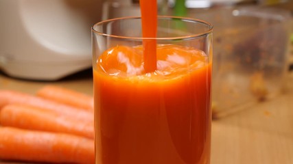 Pouring fresh squezzed carrot juice iinto glass. Healthy food, natural source of vitamin a. Slow motion - Powered by Adobe