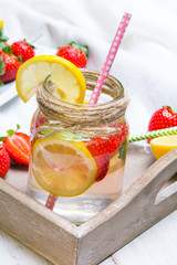 Mineral  water with fresh strawberries, lemon  and mint in jar on a white wooden background, copy space