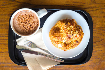 Top view, almond croissant and hot chocolate on black tray.