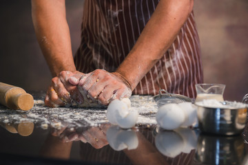 Man preparing buns at table in bakery, Man sprinkling flour over fresh dough on kitchen table