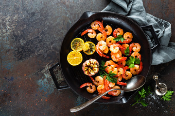 Prawns roasted on grill frying pan with lemon and garlic. Grilled shrimps, prawns. Seafood. Top view. Dark background