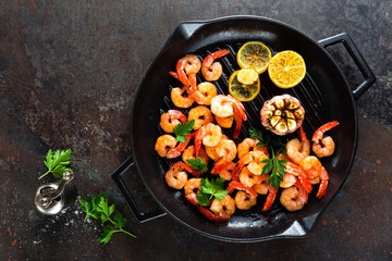 Prawns roasted on grill frying pan with lemon and garlic. Grilled shrimps, prawns. Seafood. Top view. Dark background