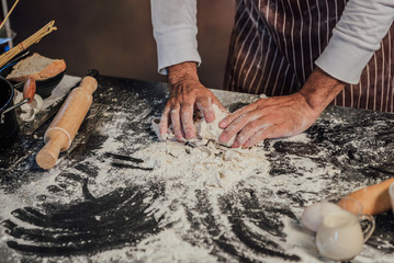 Man preparing buns at table in bakery, Man sprinkling flour over fresh dough on kitchen table