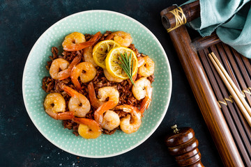 Prawns roasted on grill and boiled brown rice on plate. Grilled shrimps, prawns with rice. Seafood. Asian cuisine. Top view. Dark background