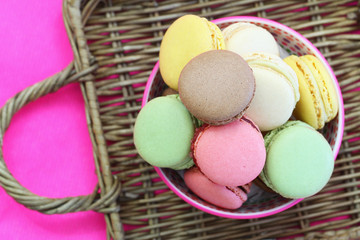Selection of colorful macaroons in bowl on wicker surface
