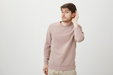 Portrait of handsome european male holding hand near ear, expressing interest while overhearing...