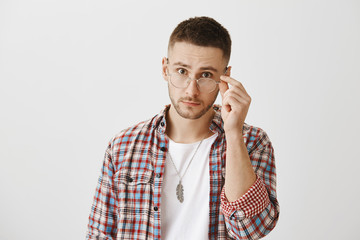 You really mean what you said. Surprised or questioned attractive student taking off trendy glasses and looking at camera as if being stunned with sudden question or revelation over gray wall