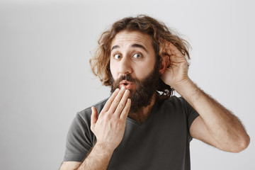 Curious man eavesdropping behind door. Studio shot of handsome intrigued eastern guy who likes...