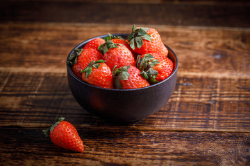 Fresh tasty strawberries in a black cup on a wooden table. Strawberry on the table next to cup of berry.