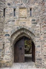 Dornie, Scotland - June 10, 2012: Closeup of gray-stone bowed entrance to Eilean Donan Castle with beige coat of arms above. Brown door open showing some green vegetation.