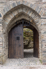 Fototapeta na wymiar Dornie, Scotland - June 10, 2012: Closeup of gray-stone bowed entrance to Eilean Donan Castle. Brown door open showing some green vegetation.