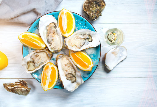 Fresh oysters close-up on blue plate, served table with oysters, lemon and champagne in restaurant. Gourmet food. Tabletop view