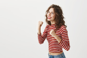 You should not tell me I gained weight. Studio shot of pieces off attractive woman raising fists and smiling, being ready to punch boyfriend who asked for it with his bad behavior over gray background