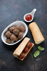 Homemade subs with baked beef meatballs on a dark brown stone background, elevated view, studio shot