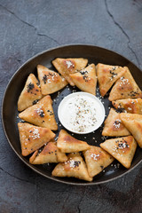 Meat samosas served with sauce on a metal tray, cracked asphalt background, vertical shot, selective focus