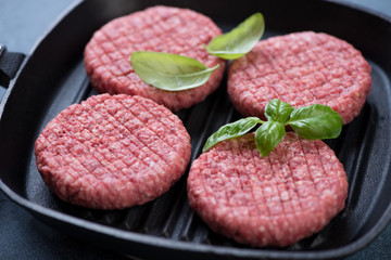 Closeup of raw fresh beef burger cutlets on a cast-iron grill pan ready to be cooked, selective focus