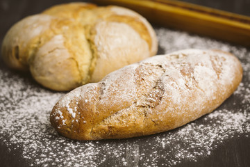 Fresh breads on dark wood with sprinkled flour.