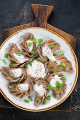 Plate of boiled rye dumplings vareniki with sauerkraut, green onion and sour cream on a wooden serving board, view from above, vertical shot