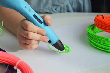 Child draws a 3D pen. The hands of the kid hold the 3D blue pen with plastic