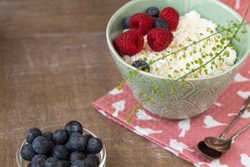 Cottage cheese in bowl with raspberries and blueberries on wooden background. Healthy breakfast .Place under the text
