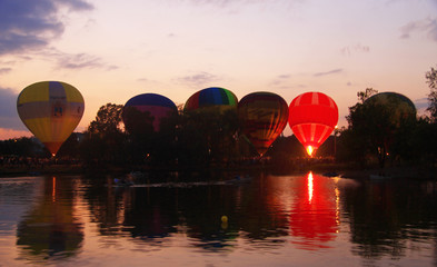 Hot air baloons flying in the evening sky near the lake