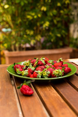 Strawberry with leaves in a green plate on a wooden table on the terrace