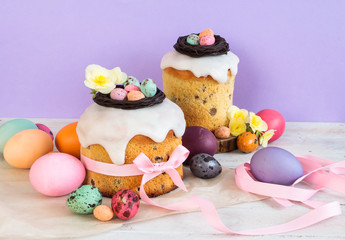 Colorful Easter spring stillife in soft light and trendy pastel colors. Traditional cake with chocolate nest, candy and qail eggs decoration blossom flowers on violet background