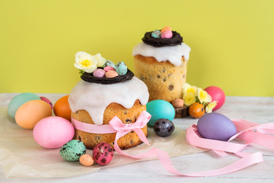 Colorful Easter spring stillife in soft light and trendy pastel colors. Traditional cake with chocolate nest, candy and qail eggs decoration blossom flowers on green background