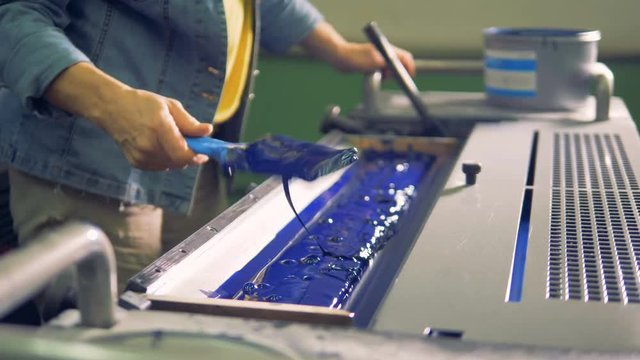 A man is leveling blue paint in a tray of a printing machine