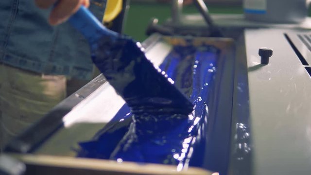 An employee is passing a brush over blue paint in a printing tray