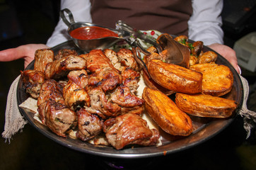 dish with potatoes and barbecue in the hands of the waiter