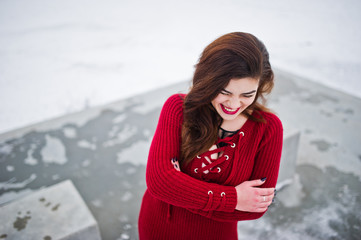 Brunette plus size model at red against frozen lake on winter day.