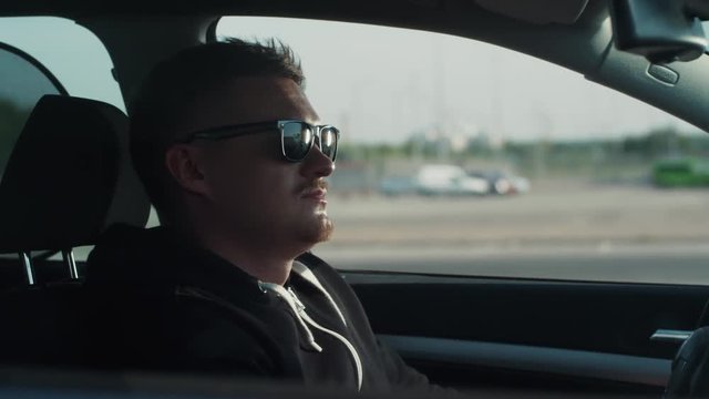 Young bearded man in sunglasses sits in the car, tries to steal it and turn it on without keys, nothing works out, he is caught on the crime scene. Carjacker, crossing the boundaries of law.