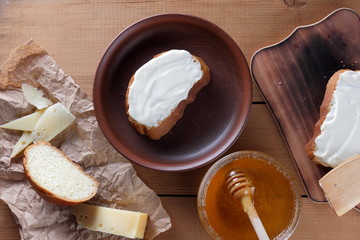 Cheese on a wooden board, food on parchment paper, sandwiches with soft cheese, honey in glass dishes, copy space, cheese pattern, wood background, wooden cutlery, simple food, art