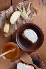 Cheese on a wooden board, food on parchment paper, sandwiches with soft cheese, honey in glass dishes, copy space, cheese pattern, wood background, wooden cutlery, simple food, art
