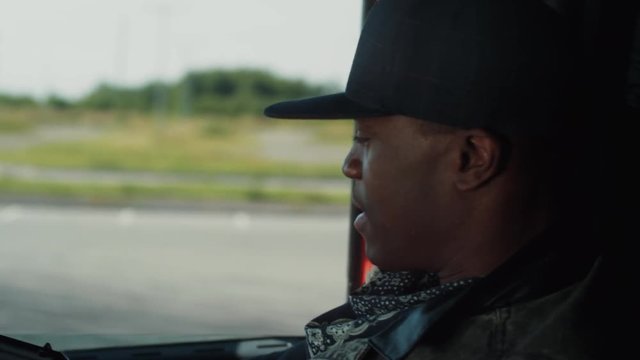 Close up view of a young armed Afro-American getting in the stolen truck, speaks with his accomplice and actively gesturing with handgun, happily smiling because of successfully finished robbery.