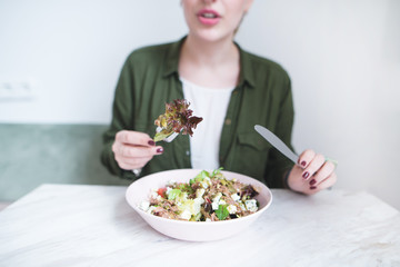 Salad greens tied to the fork close up. Girl's hands with a knife and a fork over a salad plate. Healthy Eating. The girl eats a salad