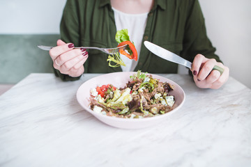 A woman eats a healthy meal for breakfast. Girl and plate of salad on the table. Healthy Eating. A fork with vegetables in a woman's hand close-up