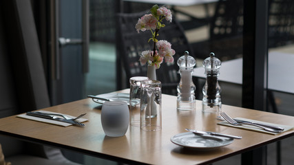 Glasses, flower fork, knife served for dinner in restaurant with cozy interior