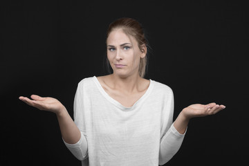 Young blond woman with arms out shrugs shoulders on black background