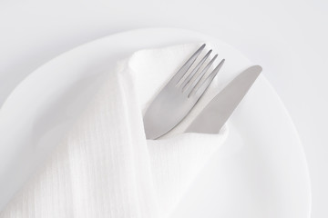 Fork and knife in white napkin on white plate