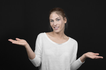 Young blond woman with arms out shrugs shoulders on black background