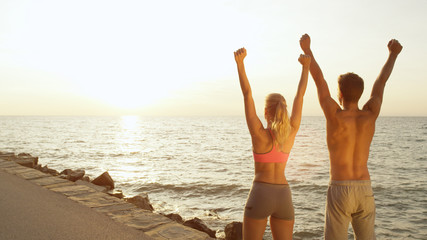 COPY SPACE: Young fit couple finishes run at the seaside and raises their arms.