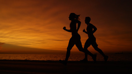 SILHOUETTE: Young woman and man go for an evening jog on a breathtaking evening