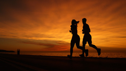 SILHOUETTE: Young man and woman doing their evening workout at gorgeous sunset.