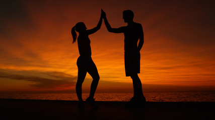 LOW ANGLE: Victorious couple high fives in beautiful orange light after workout.