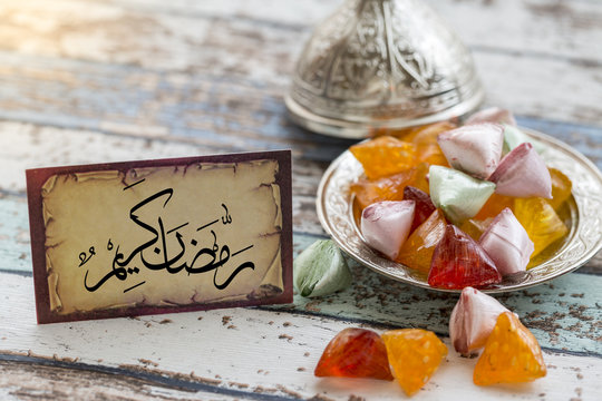 Eid mubarak text in arabic on vintage table with candies on metallic plate
