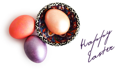 three eggs, color saucer, inscription of happy Easter on a white background.