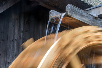The part of mill wheel rotates under a stream of water, open air museum. The wooden trough brings water to the water mill wheel. - obrazy, fototapety, plakaty