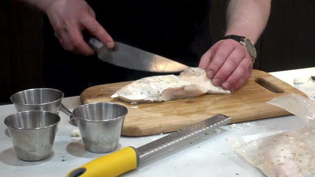 The cook cuts pieces of chicken with a knife on a wooden board. HD video